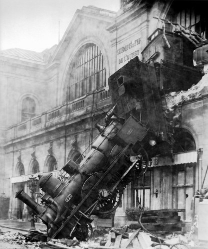 Black and white photograph of a stream locomotive that have gone bursting through the 2nd floor of a station hall following a break failure, resting with it's from on the ground and it's back towards the broken wall behind it.