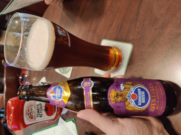 POV: you're enjoying a dark wheat lager, the Aventinus from Schneider Weiss brewery. You're holding the bottle in your left hand. The beer has been poured into a tall glass; dark brown with modest head.